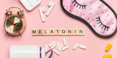 Buchstaben Melatonin, Wecker, weisse Flasche und Pillen und eine Schlafmaske auf hellem Hintergrund