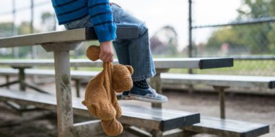 Junge, der allein auf Tribünen sitzt und Teddybär hält.