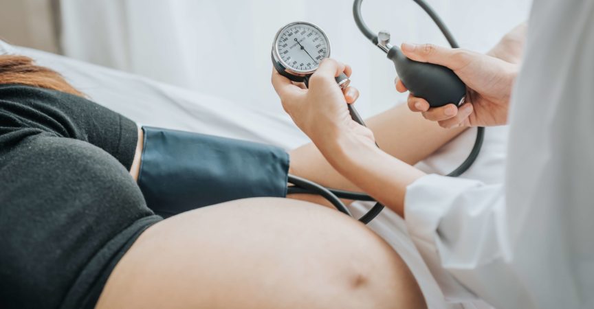 Arzt, der den Blutdruck einer schwangeren Patientin mit Blutdruckmessgerät im Bett prüft