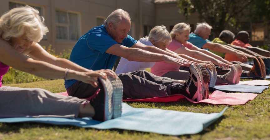 Seitenansicht der Gruppe der aktiven älteren Leute, die ihre Beine auf der Yogamatte im Park trainieren und kratzen