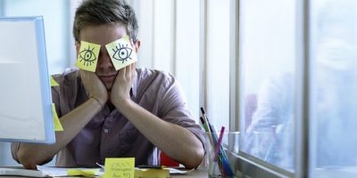 Ein junger Angestellter schläft im Büro und versteckt sich mit Posits in den Augen
