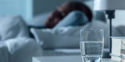 Frau, die in ihrem Bett nachts schläft, Glas auf Wasser und Pillen auf dem Vordergrund, Medizin- und Behandlungskonzept