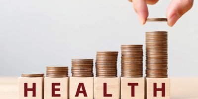 Hand, die Münzen auf Stapeltreppe als Schritt wachsendes Wachstum und Holzwürfelblock mit Wort GESUNDHEIT setzt. Investment Kranken- und Versicherungsfondskonzept