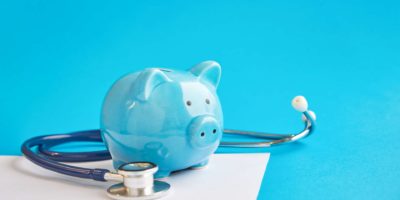 Sparschwein mit Stethoskop lokalisiert auf blauem Hintergrund. Steuervergleichskonzept. Medizinische Kostenabzüge und Steuererleichterungen