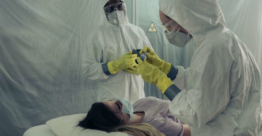 Two people attending to a woman with a virus lying on a stretcher in a field hospital