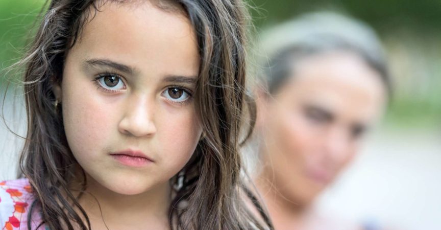 Draußen Bild eines sechs Jahre alten kleinen Mädchens des seriösen Latino, das mit ihrer Mutter im Hintergrund aufwirft