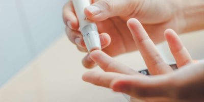 Nahaufnahme von Frauenhänden unter Verwendung der Lanzette am Finger, um den Blutzuckerspiegel durch Glukosemessgerät unter Verwendung als Medizin zu überprüfen