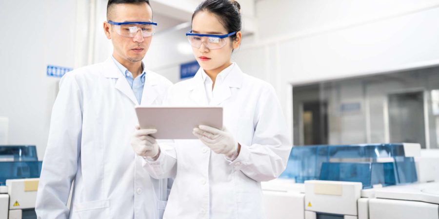 Asiatische Wissenschaftler, die eine digitale Tablette in einem medizinischen Labor verwenden.