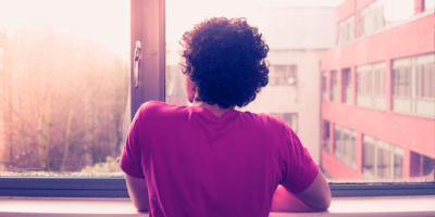 Junger Mann steht am Fensterbrett und schaut auf den Sonnenuntergang