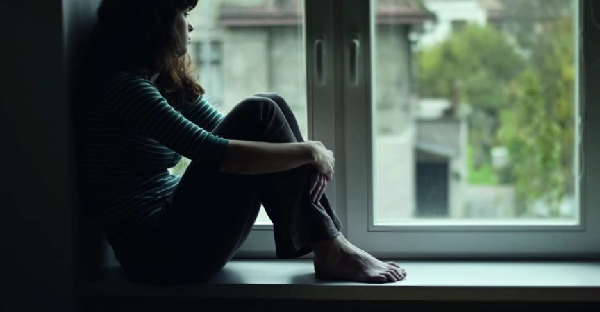Traurige junge Frau, die am Fenster sitzt
