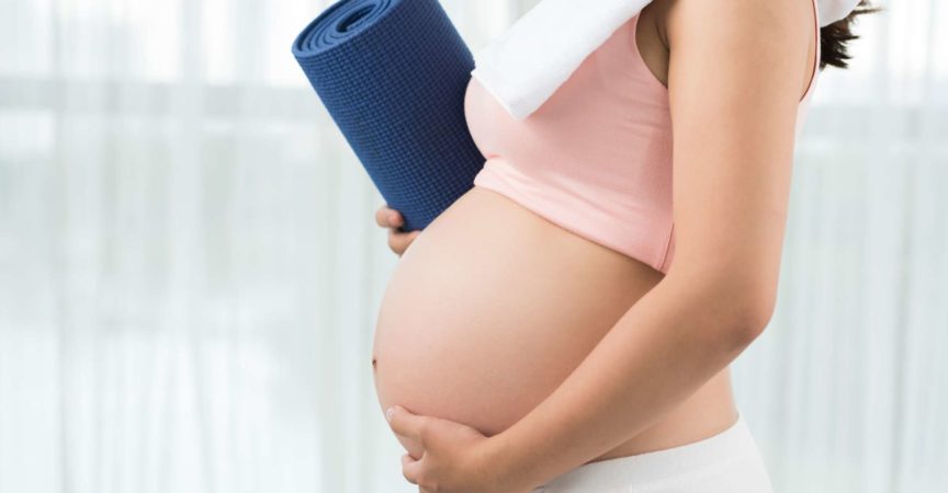 Abgeschnittenes Bild einer sportlichen schwangeren Frau mit Yogamatte