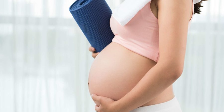 Abgeschnittenes Bild einer sportlichen schwangeren Frau mit Yogamatte