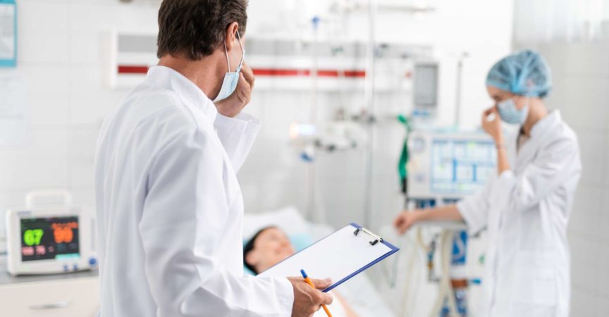 Doktor mit der medizinischen Form in der Hand, die Krankenschwester betrachtet, die nahe Patient steht
