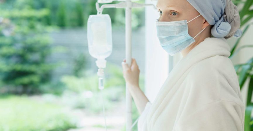 Junge Frau mit Tropf, der durch das Krankenhausfenster steht