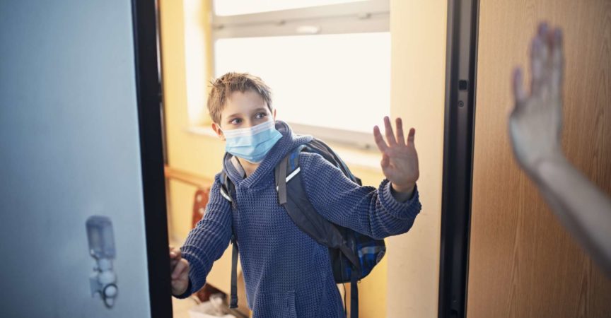 Kleiner Junge geht während der COVID-19-Pandemie zur Schule.
Mutter winkt ihm zum Abschied und er winkt zurück.
Nikon D850