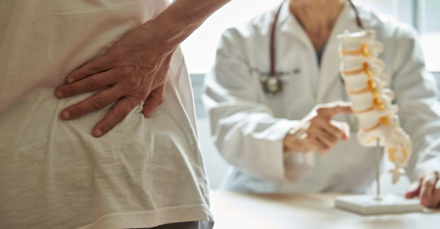 Ein männlicher Arzt erklärt der Patientin die Anatomie der Lendenwirbelsäule und klagt in der medizinischen Klinik über Rückenschmerzen