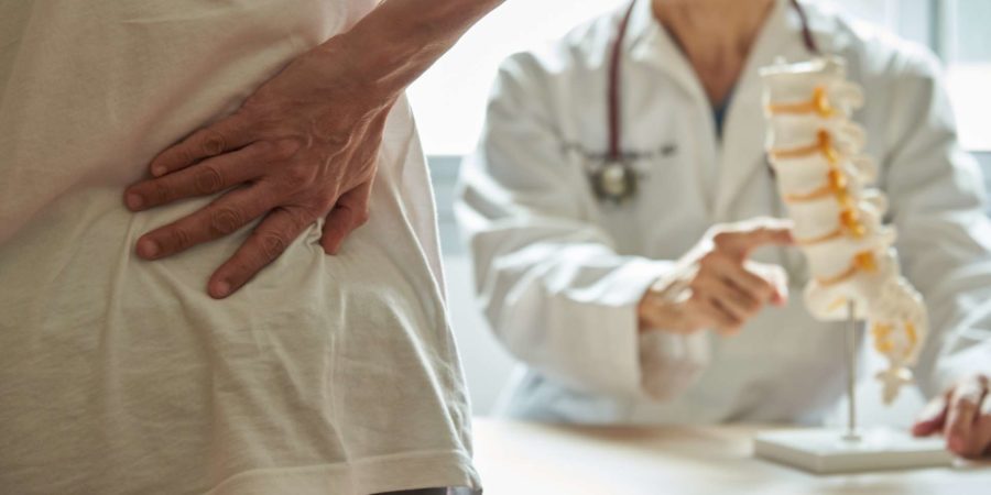 Ein männlicher Arzt erklärt der Patientin die Anatomie der Lendenwirbelsäule und klagt in der medizinischen Klinik über Rückenschmerzen