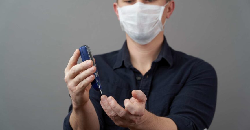 Mann, der Blutzuckerspiegel mit Glukometer auf grauem Hintergrund prüft