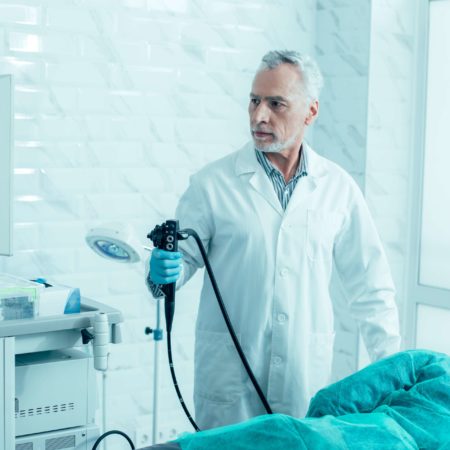 Ernsthafter reifer Arzt, der ein modernes Endoskop hält und sich auf das Verfahren vorbereitet