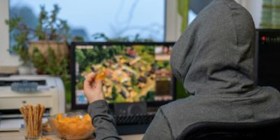 männlicher Spieler, der Strategiespiel auf Computer spielt, der Snacks isst