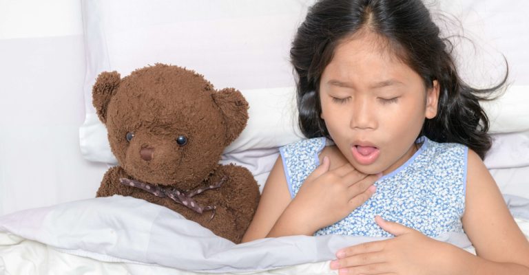 Kleines Mädchen hustet und Halsschmerzen, die auf Bett mit Spielzeugbär liegen, Gesundheitskonzept