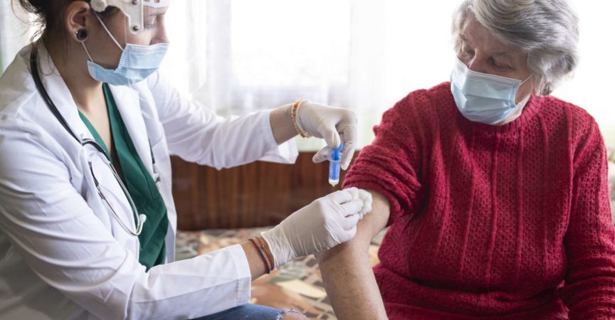 Weibliche Gesundheitsperson, die der älteren Frau in ihrem Haus Impfstoff injiziert.