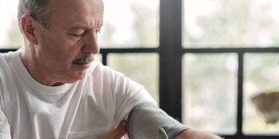 Alter hispanischer Mann, der sich schlecht fühlt, wenn er morgens ein Blutdruckgerät zu Hause verwendet, um seinen Gesundheitszustand zu überprüfen