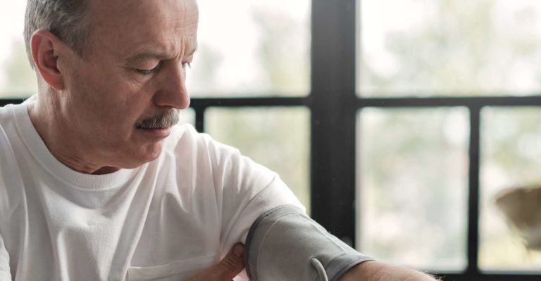 Alter hispanischer Mann, der sich schlecht fühlt, wenn er morgens ein Blutdruckgerät zu Hause verwendet, um seinen Gesundheitszustand zu überprüfen