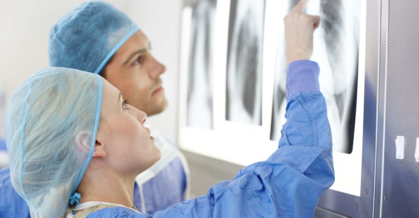 Profil einer Ärztin und eines Arztes, die über die Röntgenaufnahmen des Brustkorbs einer Patientin sprechen und darauf zeigen
