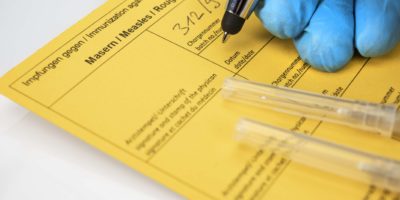Gesundheitskonzept: Hände eines Arztes mit Nitrilhandschuhen neben Spritzen und einem Impfpass. Konzept für die Diskussion um die Impfpflicht.