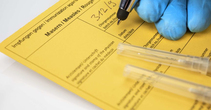 Gesundheitskonzept: Hände eines Arztes mit Nitrilhandschuhen neben Spritzen und einem Impfpass. Konzept für die Diskussion um die Impfpflicht.