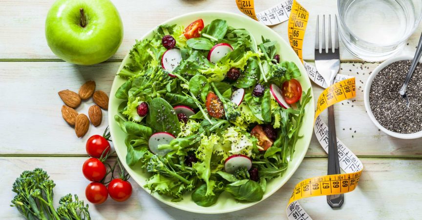 Großer frischer Salat, Apfel und Tomaten. Maßband. Frisches Gemüse. Konzept für Abnehmen und Diät. Vegane Ernährung.