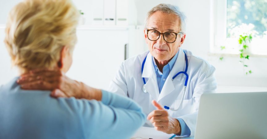 Senior Gesundheitspersonal im Gespräch mit Patientin im Krankenzimmer. Doktor, der der älteren Frau zuhört, die Rückenschmerzen hat.