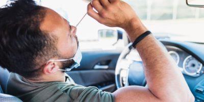 Während er in seinem Auto sitzt, führt ein Mann im mittleren Erwachsenenalter einen Selbst-COVID-Test auf einer Fahrt durch die COVID-Teststelle durch.