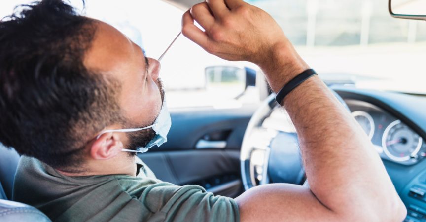 Während er in seinem Auto sitzt, führt ein Mann im mittleren Erwachsenenalter einen Selbst-COVID-Test auf einer Fahrt durch die COVID-Teststelle durch.