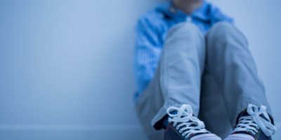 Trauriger Junge in Turnschuhen mit Asperger-Syndrom sitzt alleine in seinem Zimmer