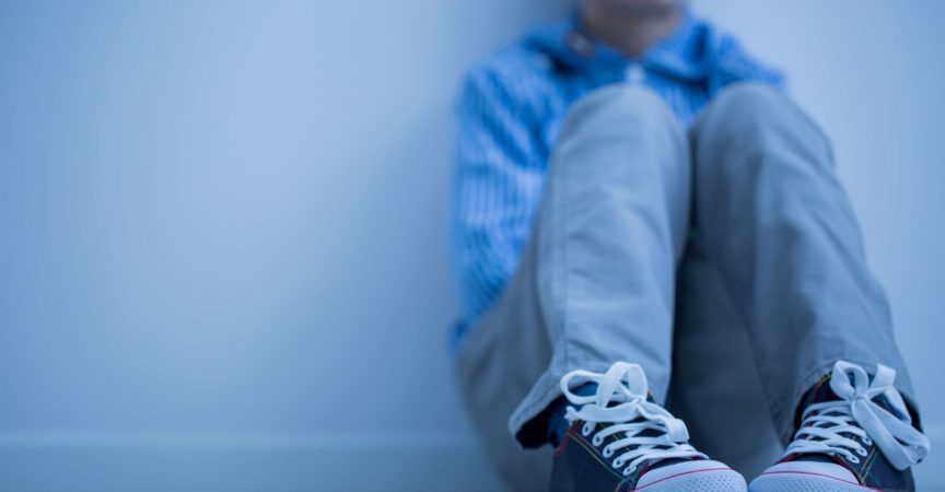 Trauriger Junge in Turnschuhen mit Asperger-Syndrom sitzt alleine in seinem Zimmer