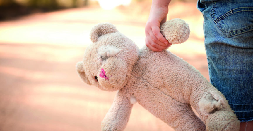 Farbiges Foto auf Lager eines kleinen außer Kontrolle geratenen Mädchens, das einen alten Teddybär an der Seite einer unbefestigten Straße im ländlichen Land hält.