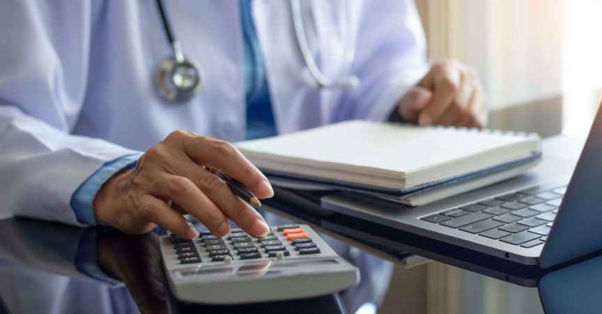 Ärztin mit Taschenrechner und Notebook am Schreibtisch im modernen Büro in der Klinik oder im Krankenhaus