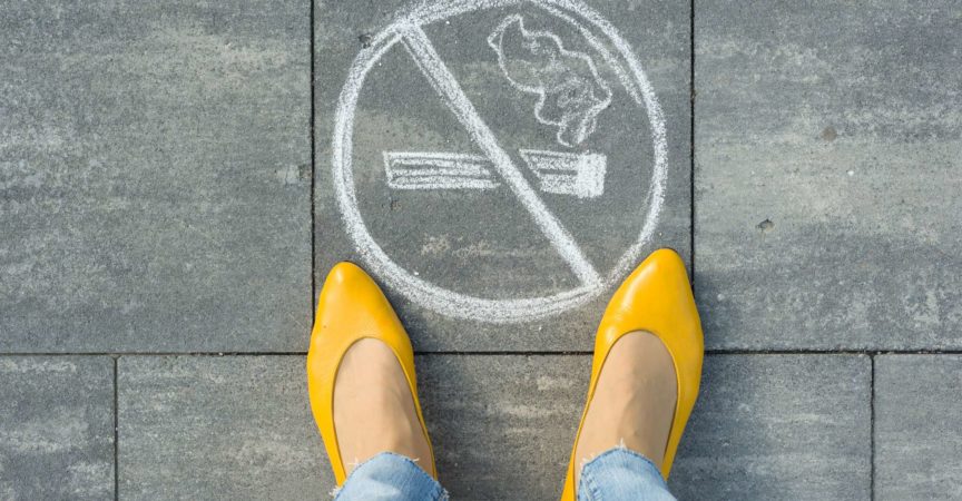 Female feet with picture no smoking painted on the grey sidewalk.