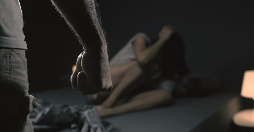 Mann bedroht eine Frau im Schlafzimmer, sie hat Angst und liegt im Bett, häusliche Gewalt Konzept