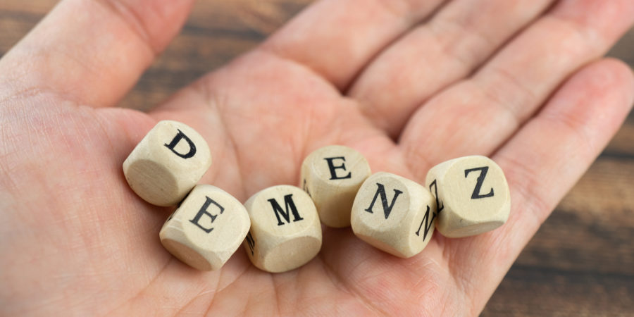 Hand with wood cubes and the German word for dementia, wooden background
