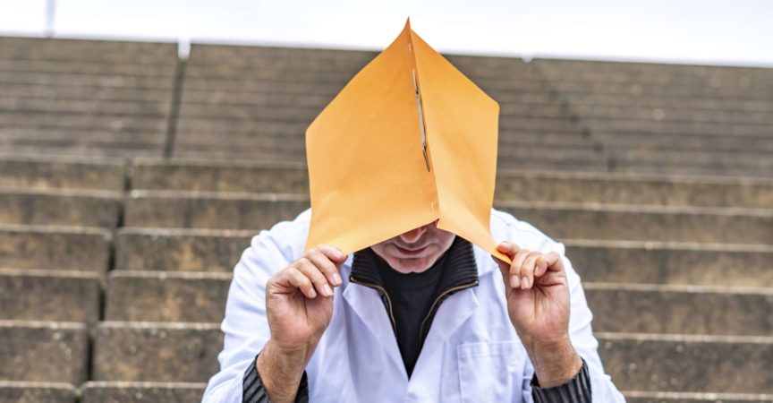 Arbeitsproblem. Allgemeinmediziner oder Zahnarzt, der auf einer Außentreppe sitzt und sein Gesicht mit einer klinischen Studie versteckt