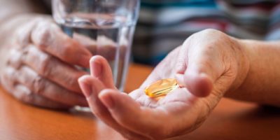 Omega-3-Pille und Glas Wasser in älteren weiblichen Händen. Medizin- und Gesundheitskonzept mit Menschen