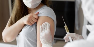 Arzt in persönlichem Schutzanzug oder PSA injiziert Impfstoff, um die Immunität einer Patientin zu stimulieren, bei der das Risiko einer Coronavirus-Infektion besteht. Coronavirus, Covid-19 und Impfkonzept