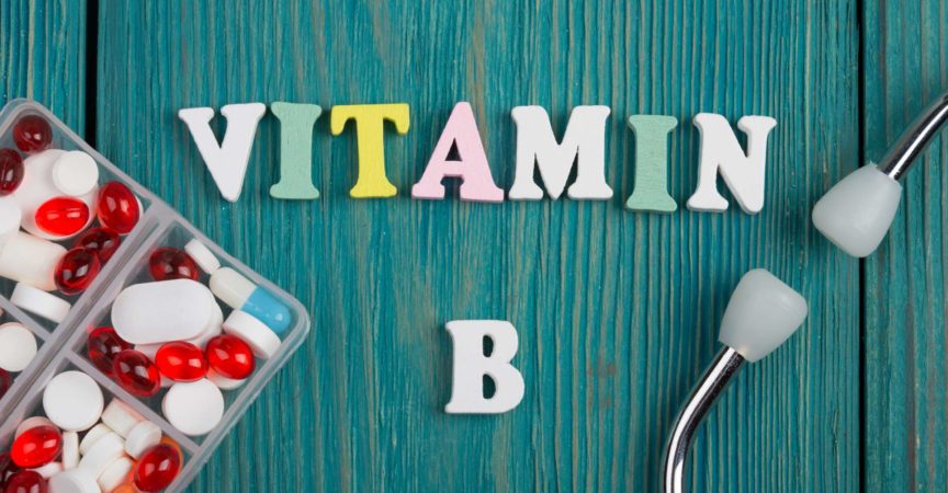 Text "Vitamin B" aus farbigen Holzbuchstaben, Stethoskop und Pillen auf blauem Holzhintergrund