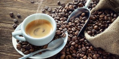 Tasse Espresso mit Kaffeebohnen, Beutel, Schaufel und Dampf auf rustikalem hölzernem Hintergrund