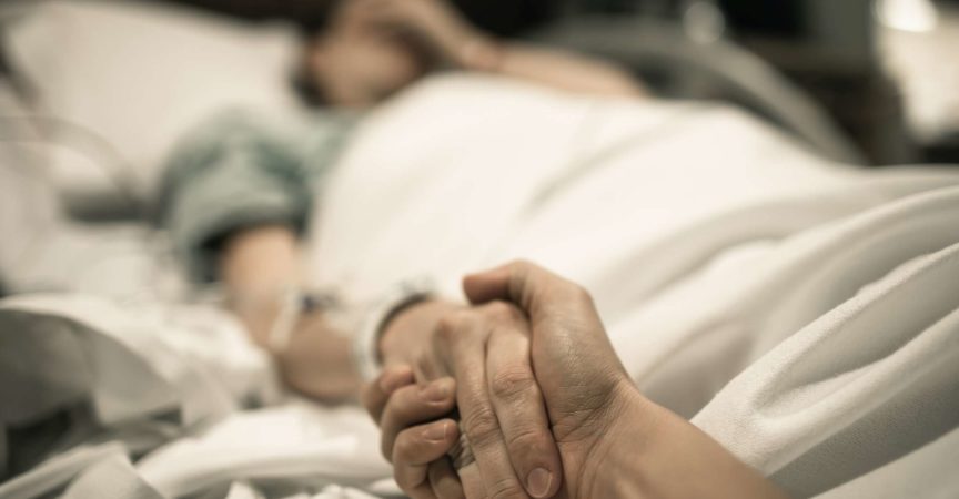 Kranke Frau, die im Krankenhausbett mit der Hand liegt, die von der Liebe eins gehalten wird. Familienlinien und medizinisches Tragödienkonzept.