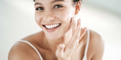 Lächelnde junge Frauen, die Feuchtigkeitscreme auf ihr Gesicht auftragen
