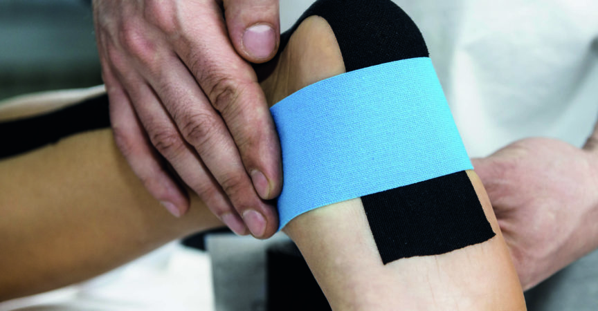 Physiotherapeut legt Tape am Fuß des Patienten an